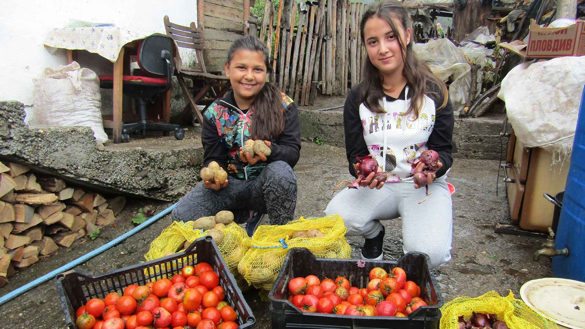 Two girls with trays of vegetables.